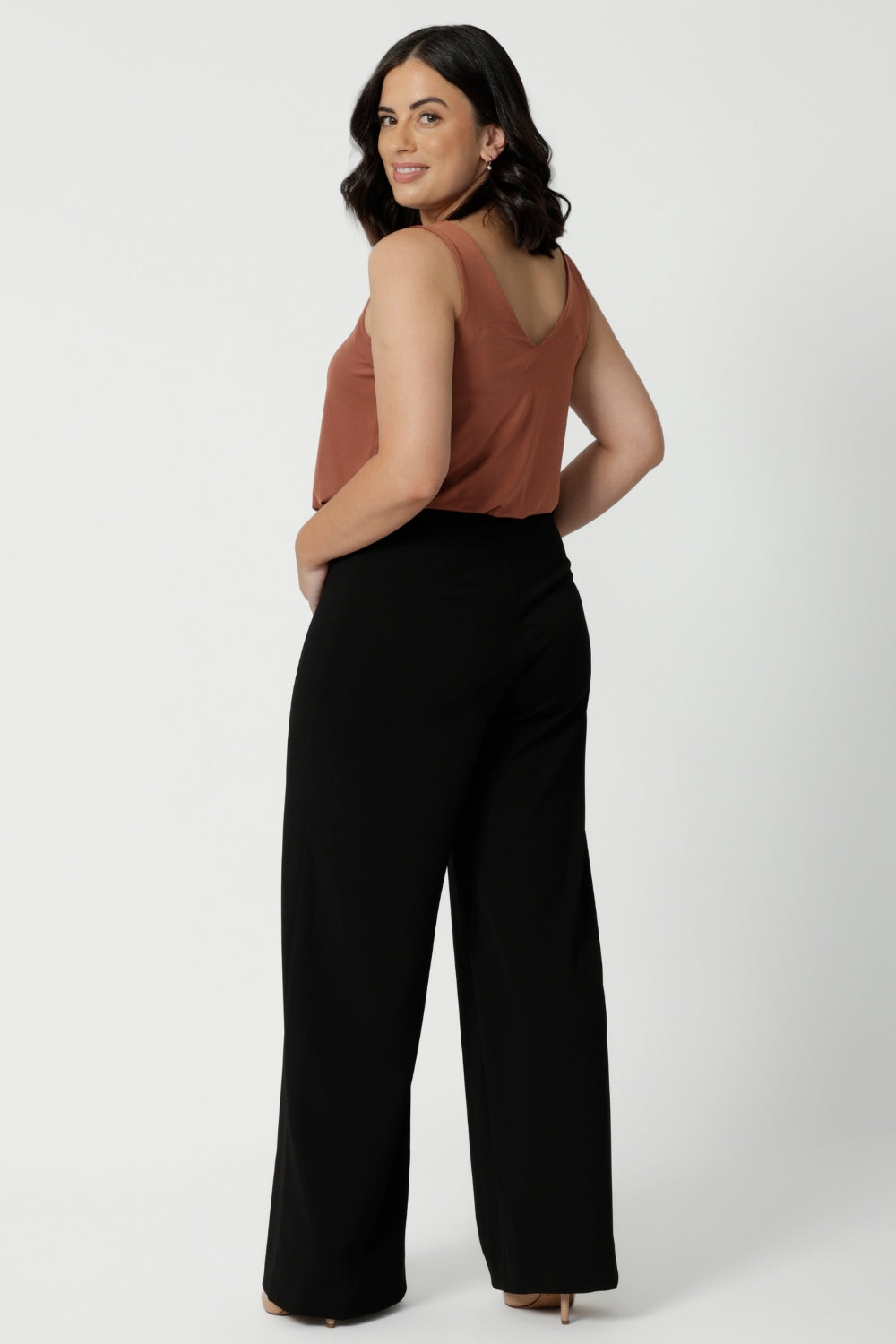 Full body back image of petite woman. wearing.black work wear pants. Easy care fabric used to craft pants is scuba crepe. Off duty pants provide breathable strech and ccomfort.  Australia Made for woman in Australia and New Zealand. Leina & Fleur is a woman’s clothing brand that has sizes ranging from 8 to 24 including plus sizes and petite sizes. 