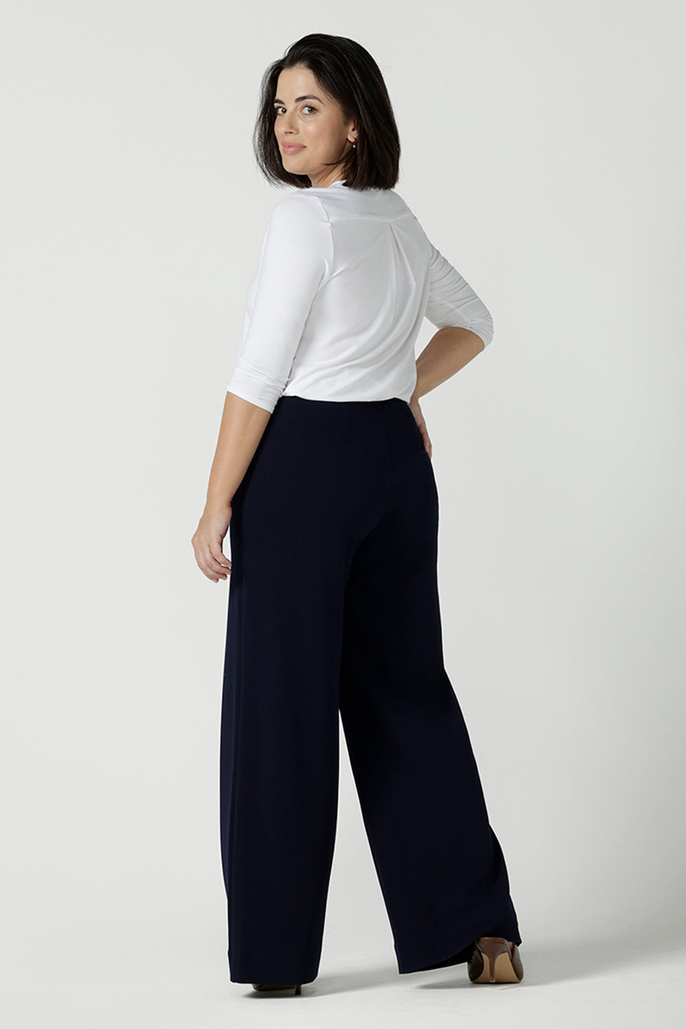 Back view of a size 10 model wears the Navy wide leg pant with navy scuba crepe. High waisted and tailored with belt loops. Stylish and corporate workwear for women size 8 - 24. Made in Australia. Styled back with a white Jaime top in soft bamboo.