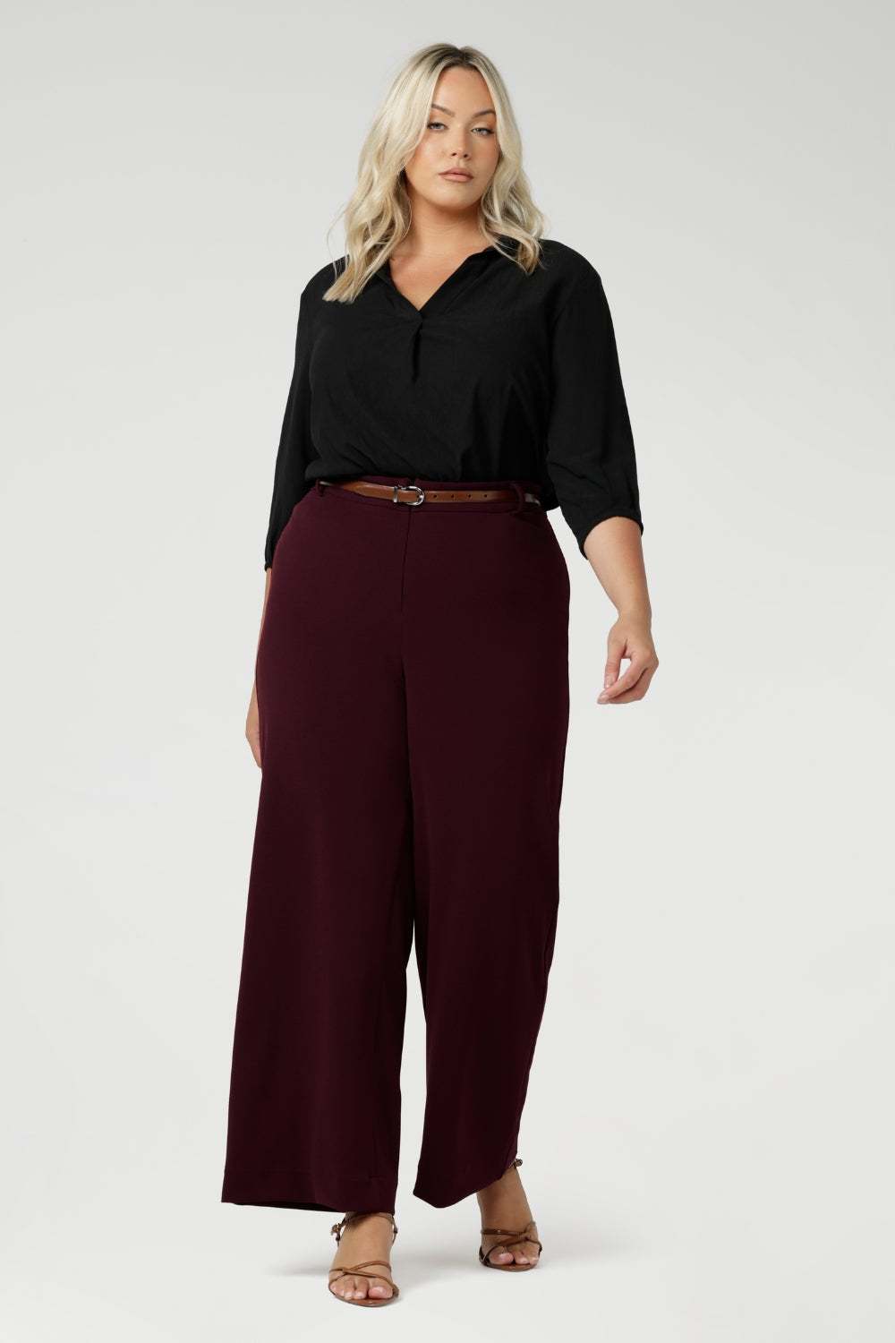 The high-rise design offers a flattering and comfortable fit, with a waistband that includes belt loops for added styling options. The invisible front zip with an internal button ensures a sleek, streamlined look while providing a secure fit. Size 18 model wears wide leg workwear pants with black blouse.