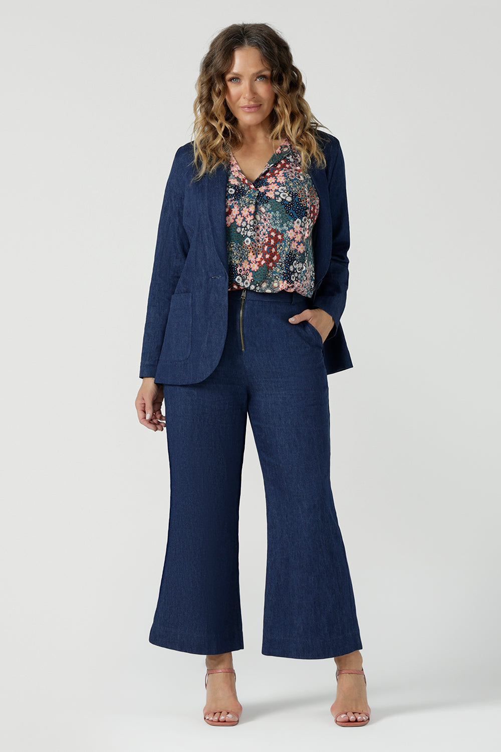 A size 10 woman wears the Bowie Top in jersey with flutter sleeves and tick neckline. Styled back with Denim Pants. Made in Australia for women size 8-24. Styled back with the Presley Pant in Whimsy. Styled with Denim Blazer and pant. 