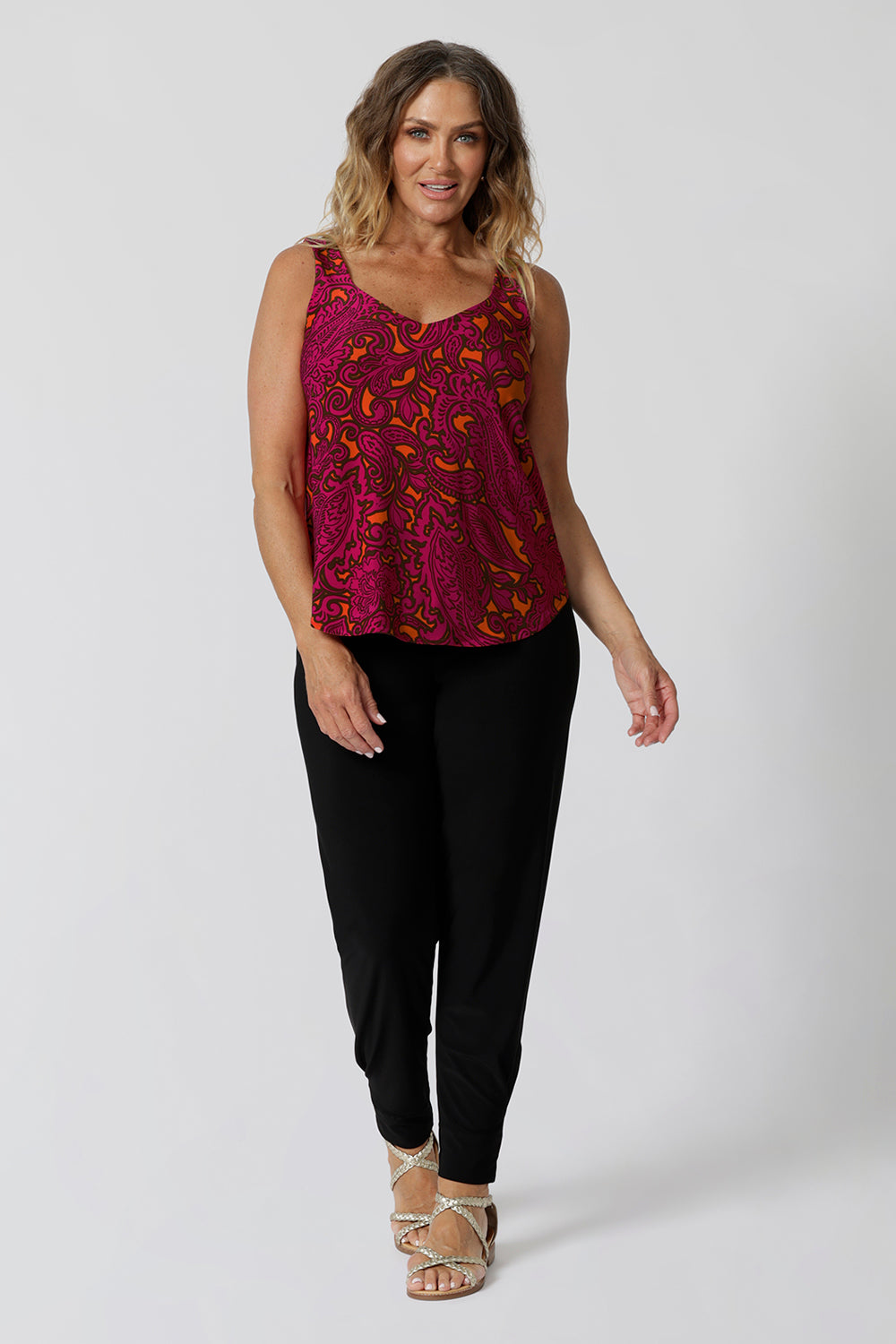 Front view of 40 year old woman wears v neck cami in a fuchsia and tangerine paisley print. Summer ready top is sleeveless and has been crafted with soft touch jersey fabric ensuring a comfortable and cool wear.