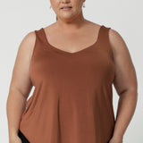 Plus sized woman wears clay coloured cami that features shirttail hemline, V cut at the front and back and wide shoulder straps. Crafted with care by Leina & Fleur, in slinky jersey fabric.