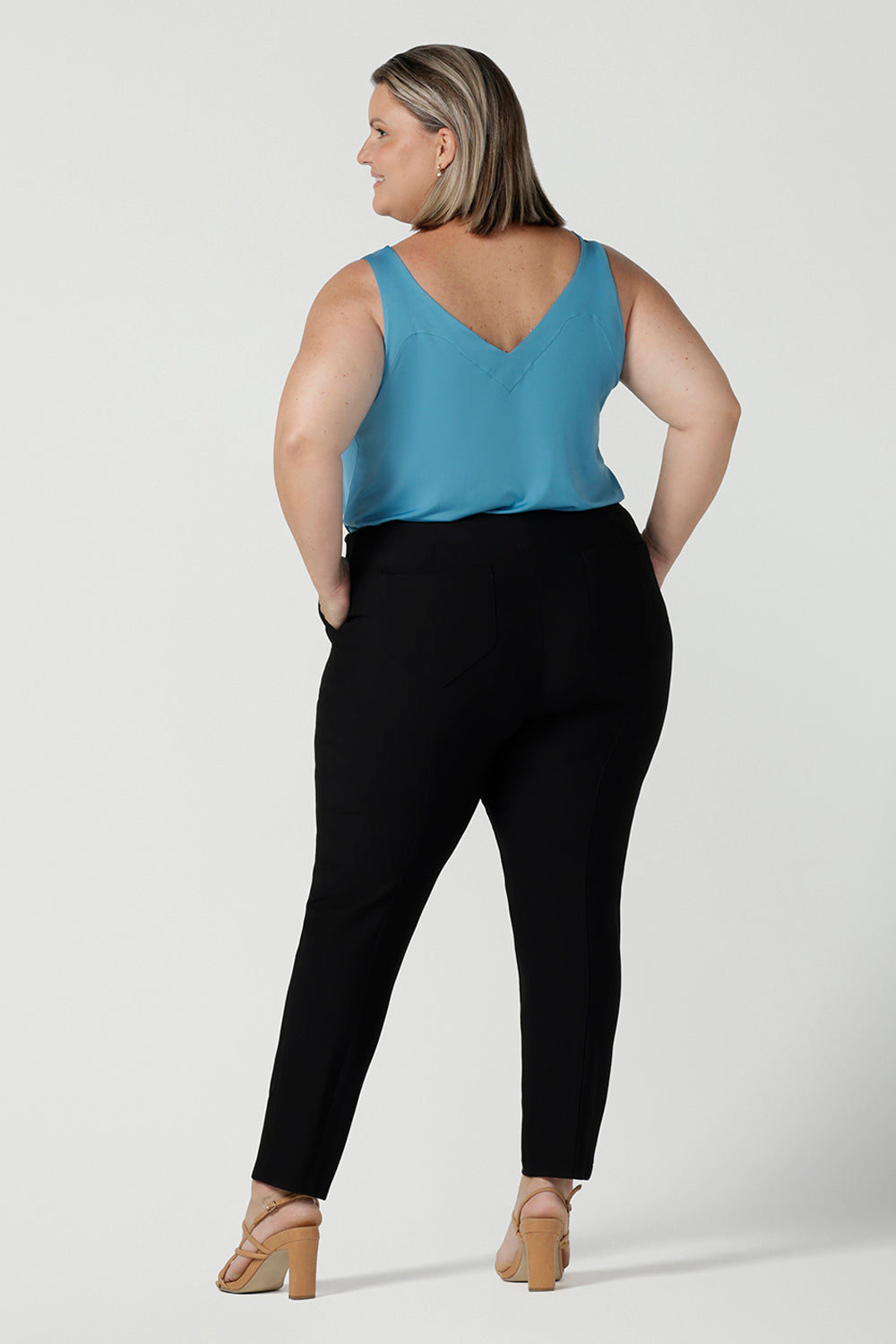 Back view of a size 18 curvy woman wears the Brooklyn pant in black. It has a slim leg and functional pockets with invisible fly front detail. Styled back with an Eddy cami in Mineral. Made in Australia for women size 8 - 24.