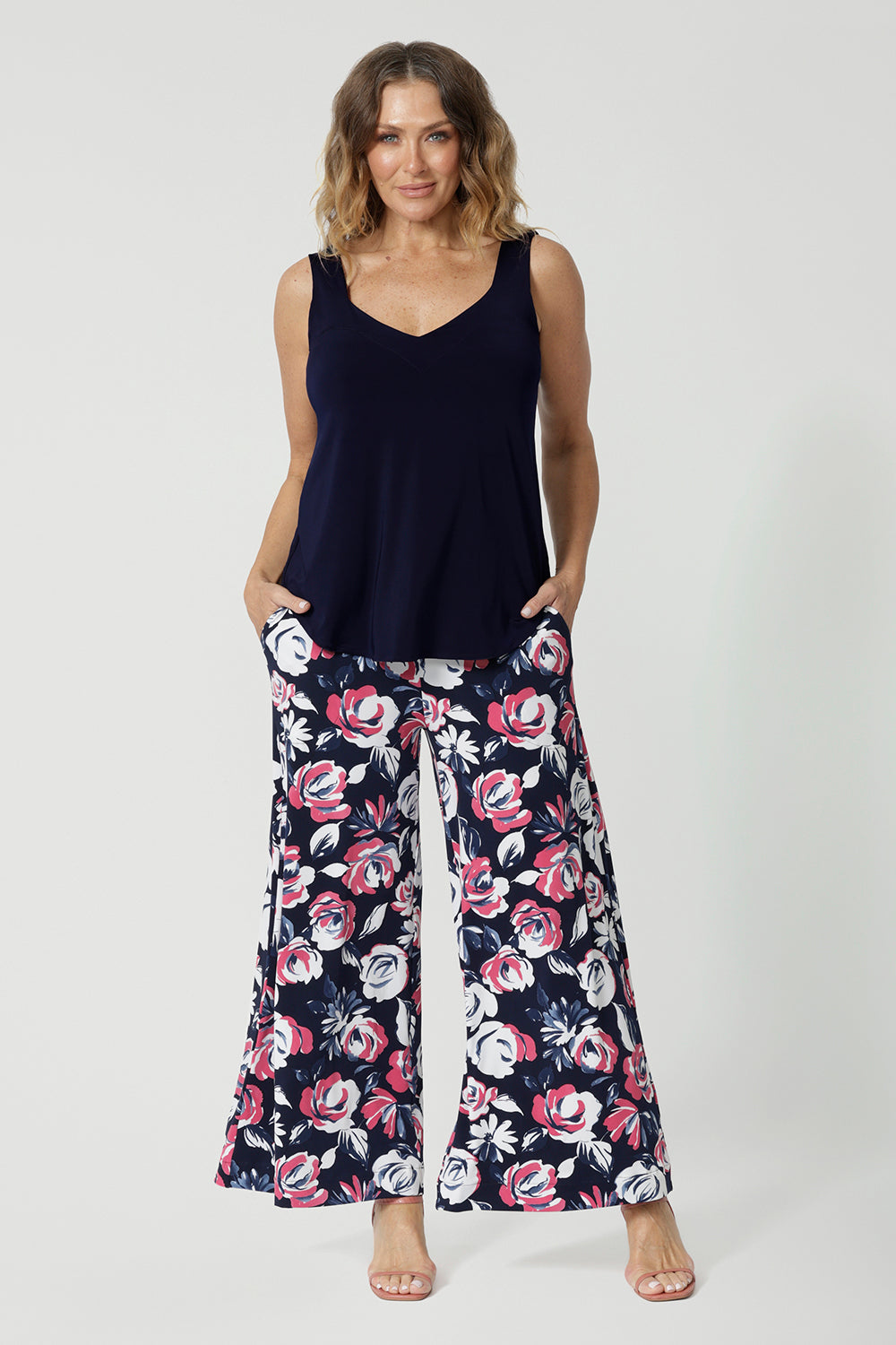 Full body shot of 40 year old woman wearing floral long pants. Made from easy care dry touch jersey fabric. Printed design has a combination of white and pink roses on navy pant base. These pants are comfortable, breathable and easy for travel. Designed in Australia by Australian and New Zealand women. Leina and Fleur is a fashion brand for woman that have sizes from 8 to 24. Shop this look now.