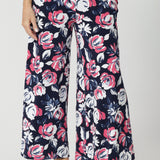 Close up front view of woman wearing wide legged pants. Floral printed pants are made of easy care dry touch jersey fabric. Colourful pants have a combination of pink and white roses on a navy pant. Pants are comfortable and perfect for travel. Fabric made in Australia by New Zealand and Australian women. Leina & Fleur is fashion brand that proudly stocks sizes from 8 to 24. Shop this fun and easy pant style in plus and petite sizes. 