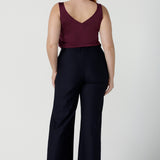 Size 12 woman wears the Eddy Cami top in Plum with wide straps. Made in Australia for women size 8 -24. style back with high waist Lulu pants in Navy. Soft tailored pants.