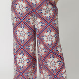 The pants are designed with a flattering high waist that elongates the legs, and they flow effortlessly into wide-leg pant, making them both relaxed and sophisticated. The geometric print, detailed in blue and red, adds a bold, graphic element to the design, with sharp lines and subtle curves that create visual interest. 