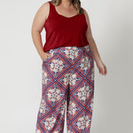 Plus sized woman wears Ellery pants in Seahorse print which displays a geometric print featuring a design mix of red & blue colours on a white base. Model pairs high waisted pants with red cami to tie the look together, matching the look with brown kitten heels. Pants available in size 8-24.