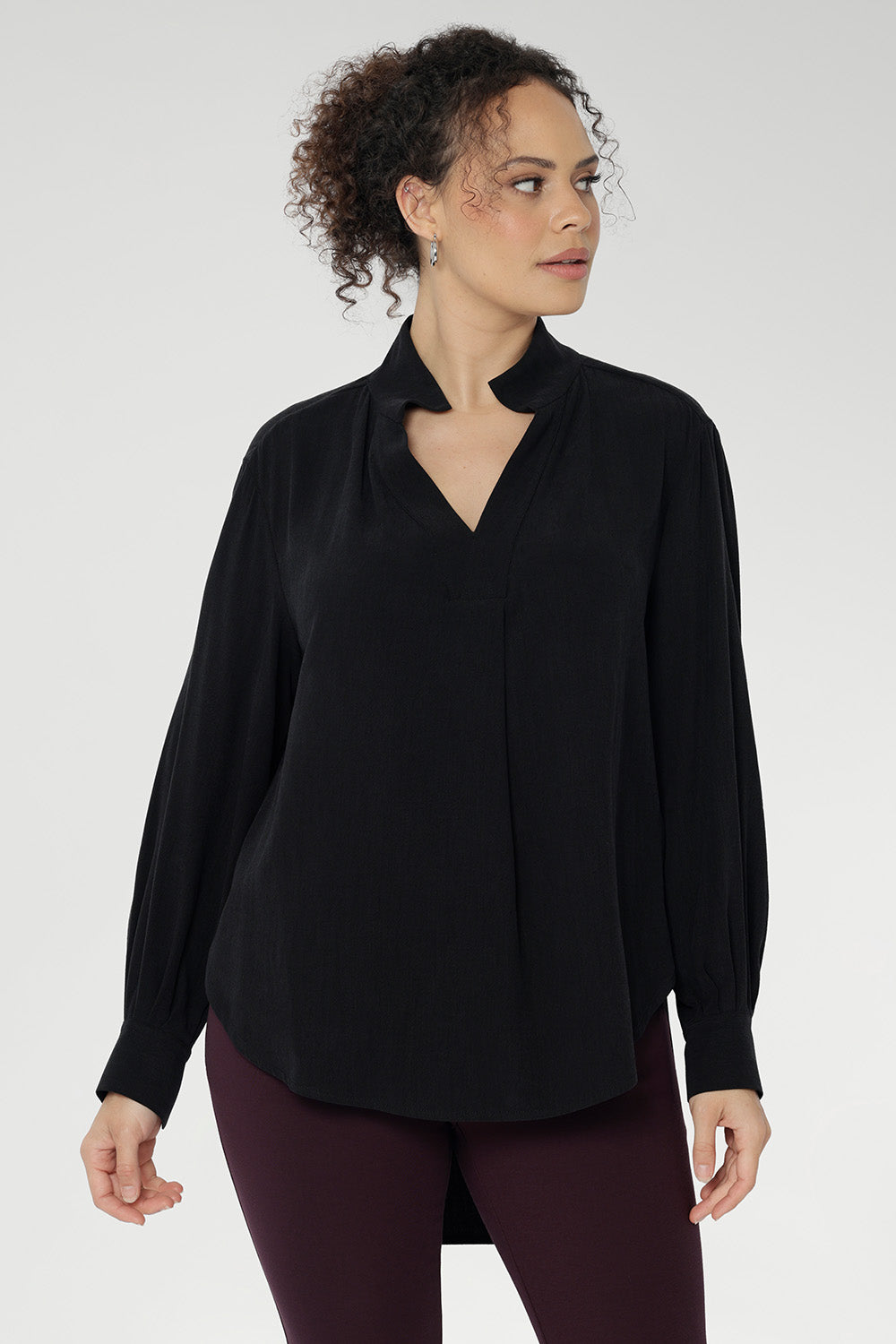A size 10 woman wears the Ellis shirt in Graphite Black styled with wine coloured skinny leg pants, cresting a corporate casual look. Available in sizes 8-24.