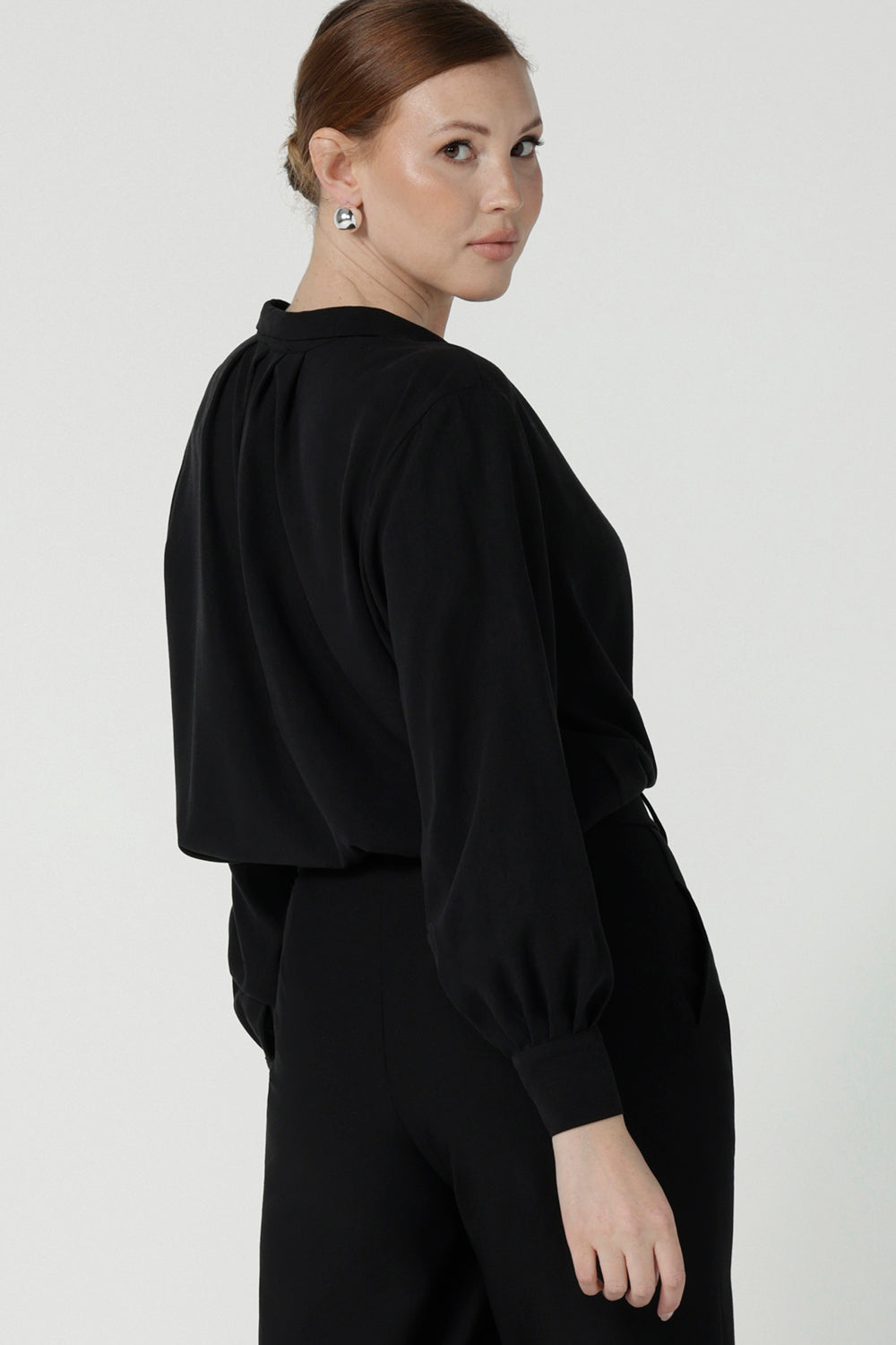 Back view of a size 10 woman wears the Ellis shirt in Graphite Black tencel. Made in Australia woven shirt in soft and breathable tencel. With cuff detail and collared neckline. Made in Australia for women size 8-24