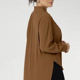 Plus size woman wears lightweight, easy to wear shirt that holds its shape without stretch. In the warm neutral shade of Nuthatch, it brings subtle sophistication to everyday dressing. The full-length sleeves are finished with clean cuffs and covered buttons — an understated touch that elevates the look. A gently curved shirttail hem sits longer at the back, offering balanced proportions and flattering coverage. Available in size 8-24.