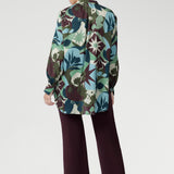 Sharp collared V-neckline and soft tailored details create a flattering shape, while full-length sleeves with covered button cuffs add a refined touch. Featuring a vibrant abstract print in rich green, blue, and plum tones, this shirt turns heads from office to evening.