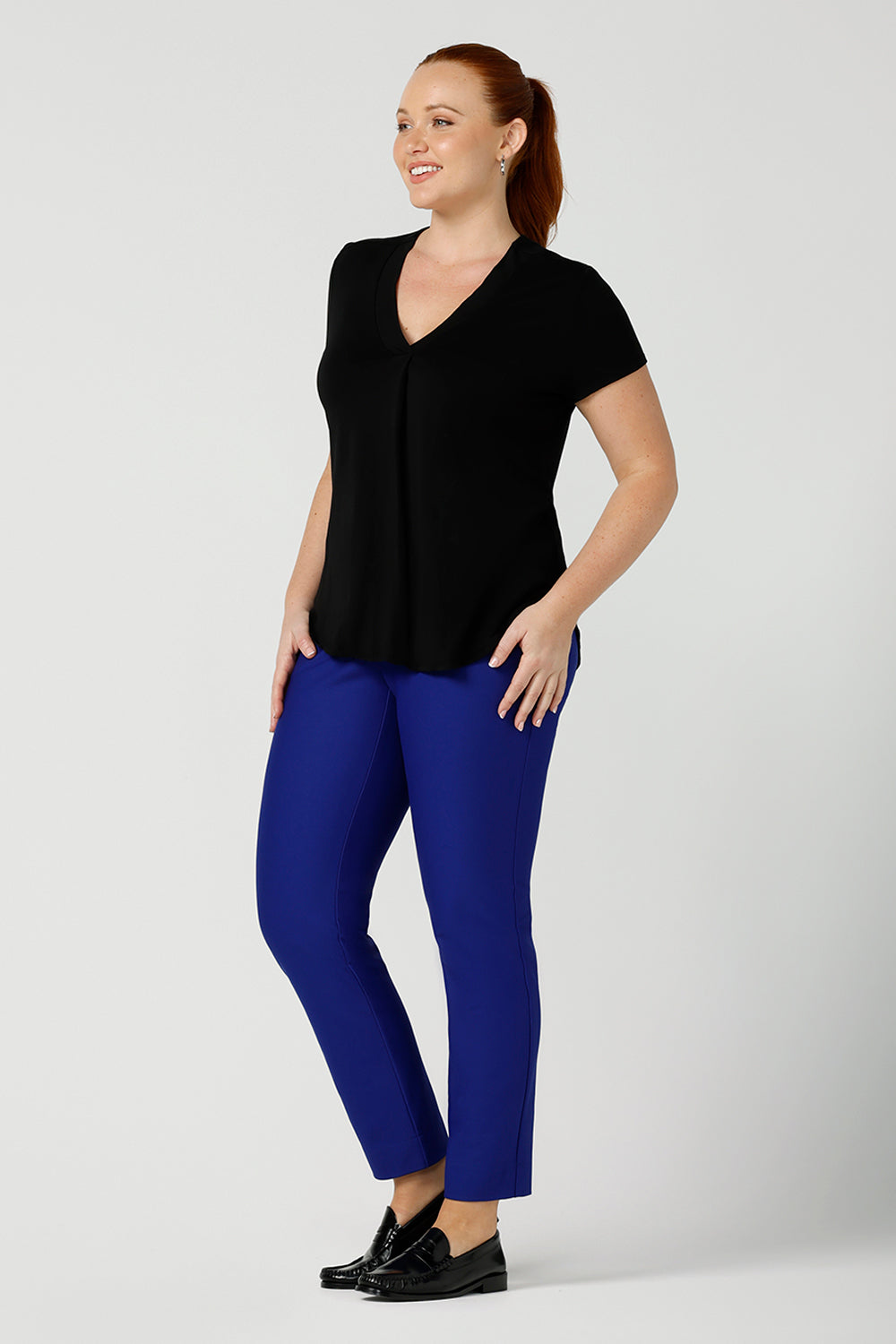 A good top for your capsule wardrobe, this V-neck black bamboo jersey top with short sleeves makes for a good office wear top for women, as well as a comfortable casual top. Worn with cobalt blue, tailored trousers and shown on a size 12 woman, this top is made for fuller figure women by Australian women's clothing brand, Leina & Fleur. Shop black tops for women in sizes 8 to 24 in their online fashion boutique.