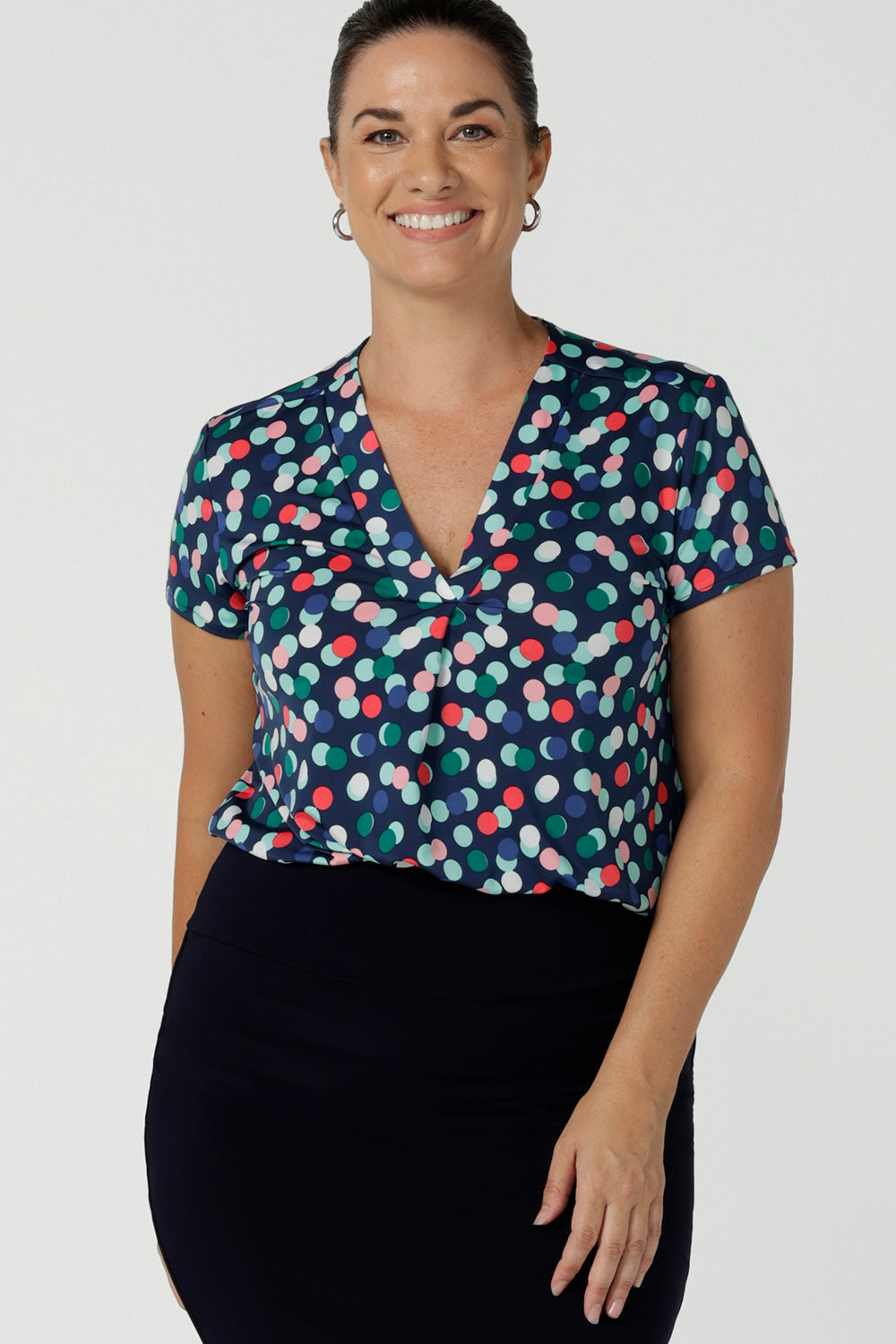 Happy corporate woman wears the Emily Top in Blue bubbles spot print. Short sleeves with a pleat front. V-neckline and back yoke. Comfortable jersey fabric. Made in Australia for women size 8 - 24.