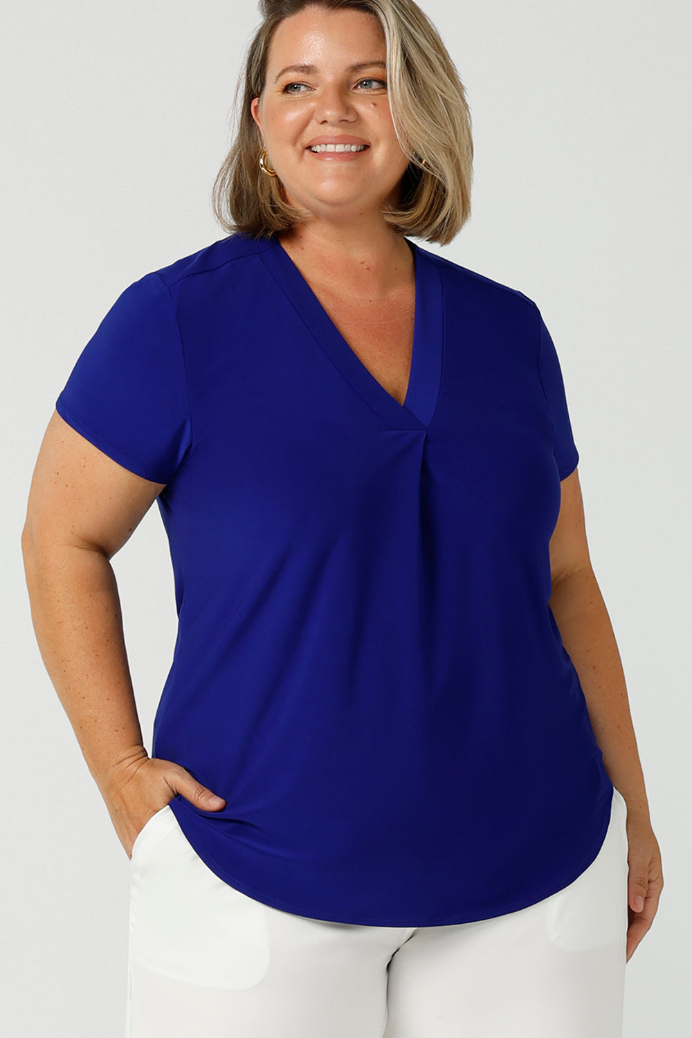 a size 18 woman wears a v-neck  jersey top in cobalt blue. She wears the top with white wide leg pants for summer. Designed and made in Australia for petite to plus size women.