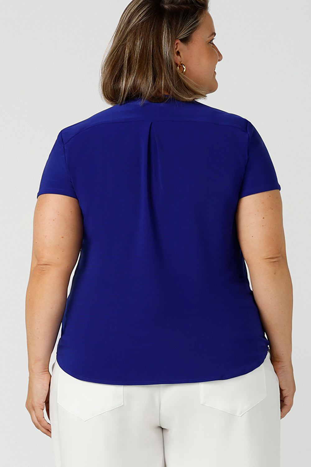 Back view of a size 18 woman wears a v-neck  jersey top in cobalt blue. She wears the top with white wide leg pants for summer. Designed and made in Australia for petite to plus size women.