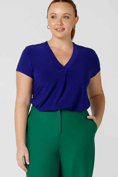 a curvy size 12 woman wears a v-neck  jersey top in cobalt blue. She wears the top with emerald green tailored wide leg pants for work or casual. Designed and made in Australia for petite to plus size women.