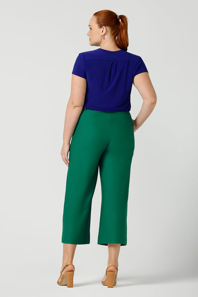 Back view of a curvy size 12 woman wears a v-neck  jersey top in cobalt blue. She wears the top with emerald green tailored wide leg pants for work or casual. Designed and made in Australia for petite to plus size women.