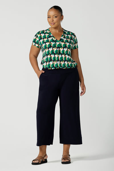 A curvy size 18 woman wearing a v-neck short sleeve jersey top in a geometric print. She wears the top with wide leg cropped pants. Designed and made in Australia for petite to plus size women.