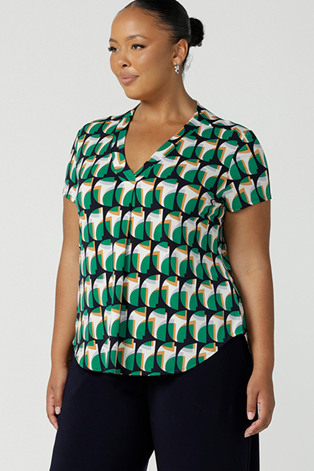 A curvy size 18 woman wears a v-neck short sleeve jersey top in a geometric print. She wears the top. Designed and made in Australia for petite to plus size women.
