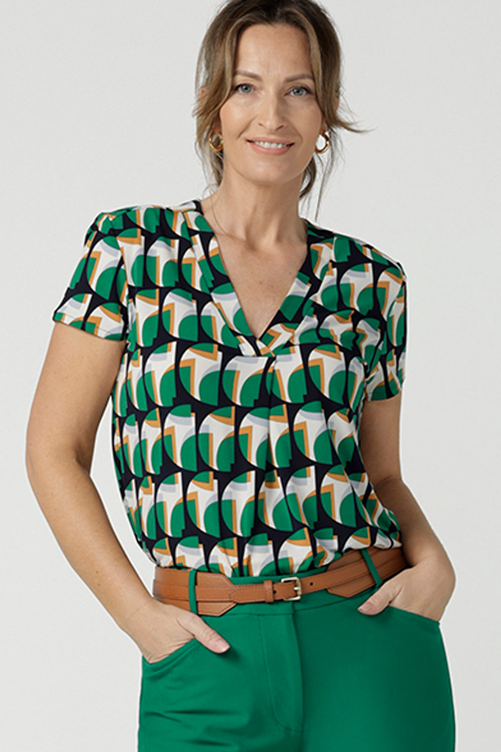 A size 10 woman wears a v-neck short sleeve jersey top in a geometric print. She wears the top. Designed and made in Australia for petite to plus size women.