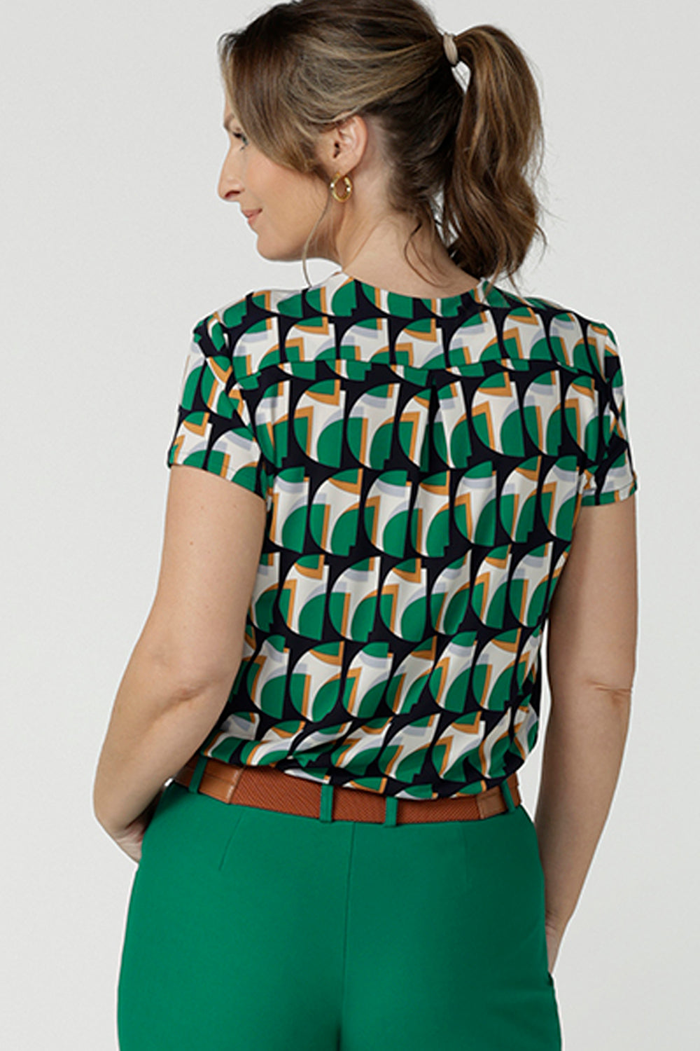 Back view of a size 10 woman wearing a v-neck short sleeve jersey top in a geometric print. She wears the top. Designed and made in Australia for petite to plus size women.