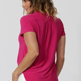 An back image of a woman in her forties wearing a hot pink work top with a v neck. Her top is made from a stretch jersey by fashion label Leina & Fleur. It is made in Australia in sizes 8 to 24.