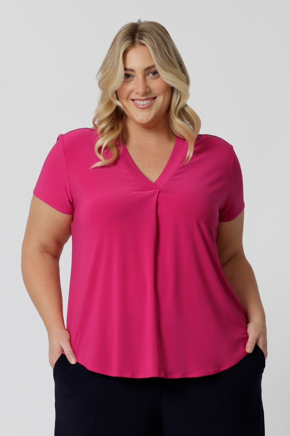 An image of a plus size woman wearing a hot pink work top with a v neck. Her top is made from a stretch jersey by fashion label Leina & Fleur. It is made in Australia in sizes 8 to 24.