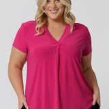 An image of a plus size woman wearing a hot pink work top with a v neck. Her top is made from a stretch jersey by fashion label Leina & Fleur. It is made in Australia in sizes 8 to 24.