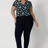 Full length shot of a good top for plus size women. A size 18, curvy woman wears short sleeve, V-neck top in aqua blue floral print. This stretch jersey top for work is worn tucked in to tapered leg, Navy blue for pants for corporate outfit, Made in Australia by Australian and New Zealand women's clothes brand, Leina & Fleur, shop curve fashion online in sizes 8 to 24.