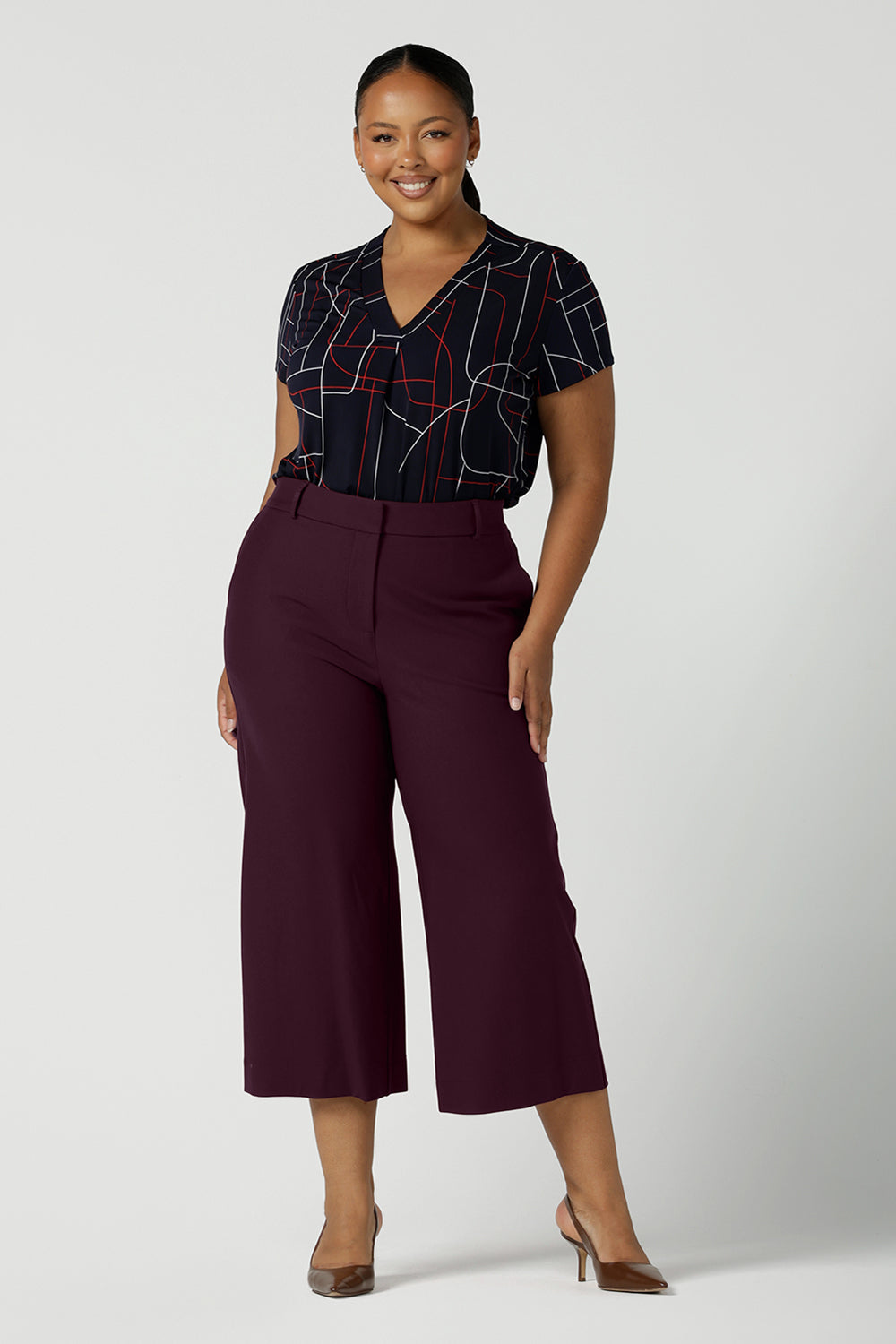 Size 12 women wears a Emily Top in Navy Abstract print. V-neckline with short sleeves on a navy base colour. Geometric print perfect for a corporate office look. Made in Australia for women size 8 - 24. Styled back with Mulberry Yael ponte pant. Soft tailored culottes. 