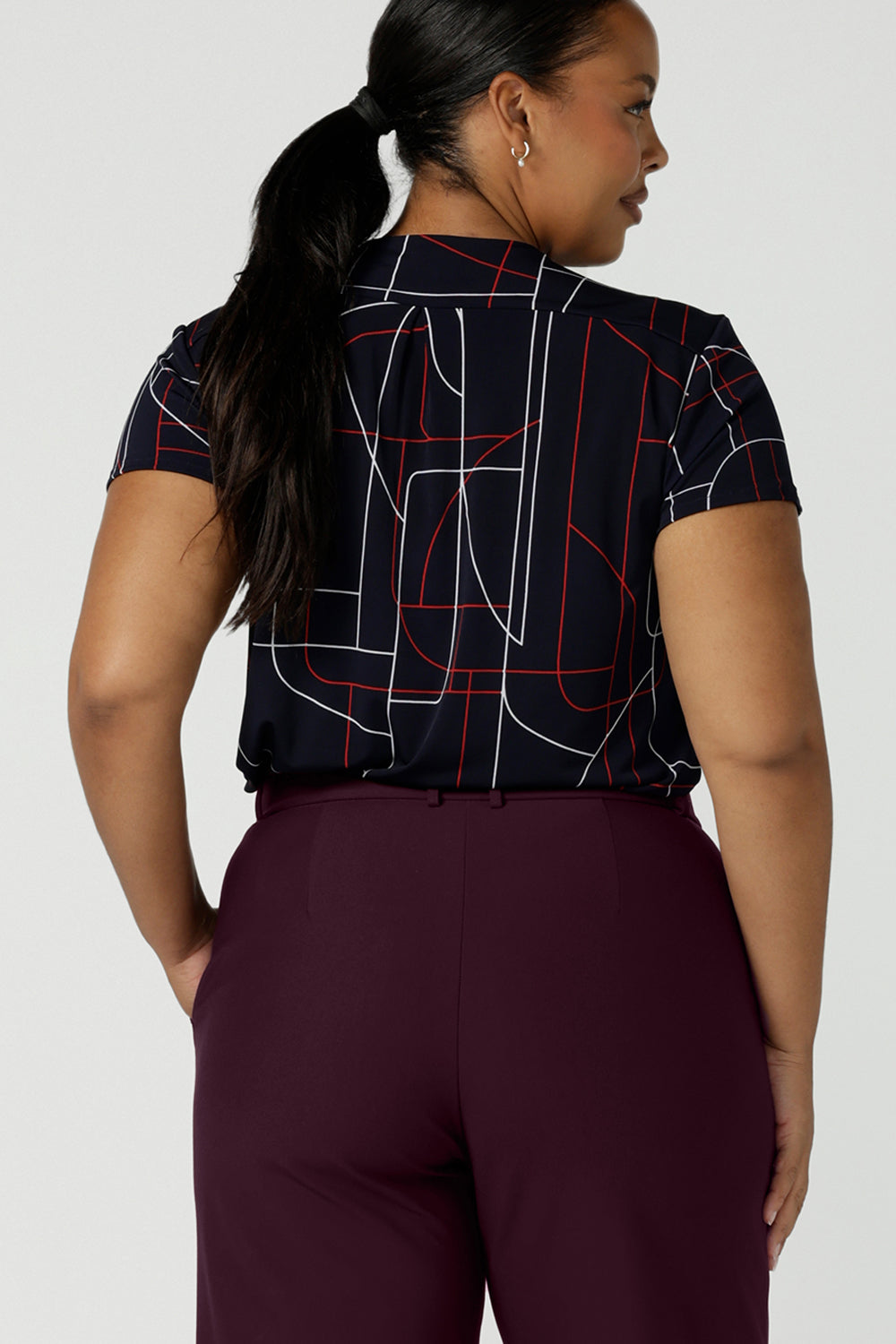 Back view of a size 16 curvy woman wears a Emily Top in Navy Abstract print. V-neckline with short sleeves on a navy base colour. Geometric print perfect for a corporate office look. Made in Australia for women size 8 - 24.