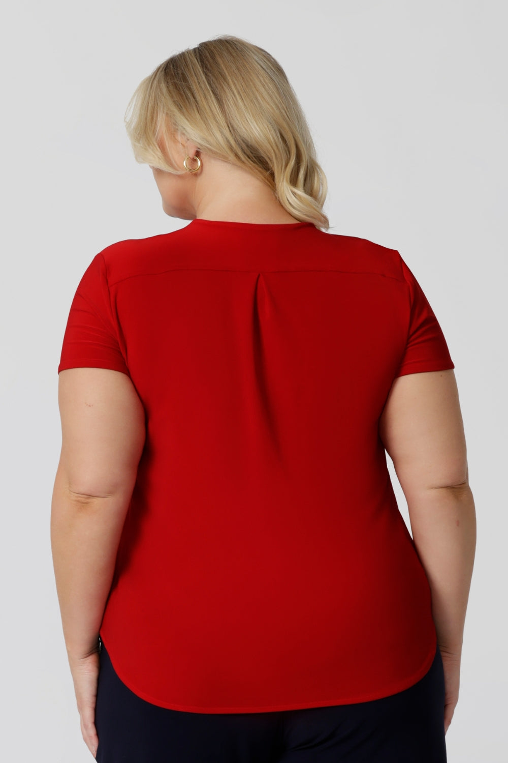 Back view of plus sized model wearing red top made of dry touch fabric that is wrinkle resistant and provides a dry, cool feel.  Fashion brand Leina & Fleur proudly sizes from 8-24.