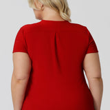 Back view of plus sized model wearing red top made of dry touch fabric that is wrinkle resistant and provides a dry, cool feel.  Fashion brand Leina & Fleur proudly sizes from 8-24.