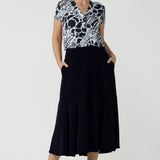 Woman wears a pull on, navy maxi skirt with ruffle hemline with a short sleeve flutter sleeve blue printed top. This black maxi skirt is a good workwear skirt or smart-casual skirt. Made in Australia in petite plus sizes 8-24.