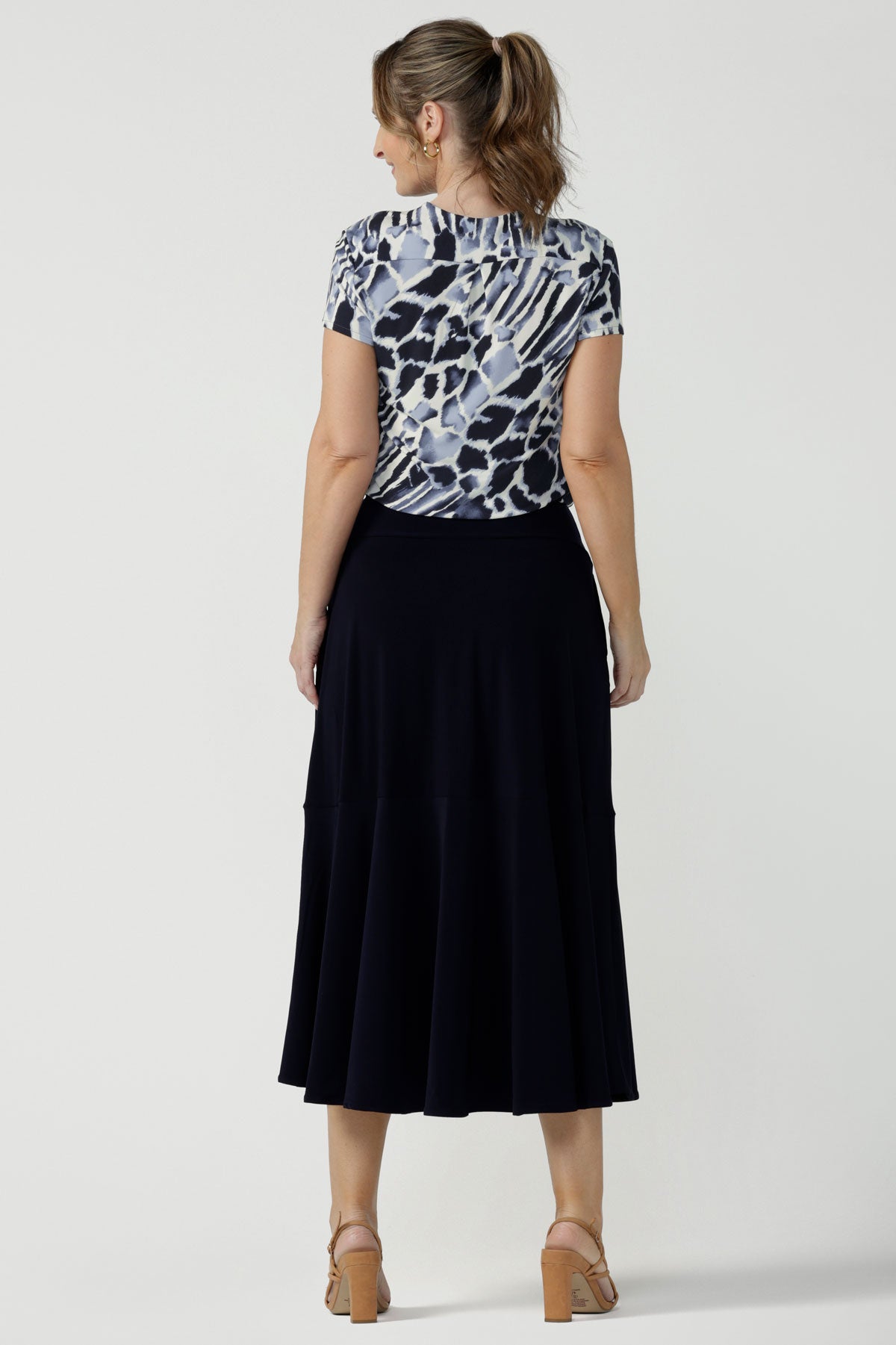 Back view of a woman wears a pull on, navy maxi skirt with ruffle hemline with a short sleeve flutter sleeve blue printed top. This black maxi skirt is a good workwear skirt or smart-casual skirt. Made in Australia in petite plus sizes 8-24.