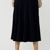 Back view of a woman wears a pull on, navy maxi skirt with ruffle hemline with a short sleeve flutter sleeve blue printed top. This black maxi skirt is a good workwear skirt or smart-casual skirt. Made in Australia in petite plus sizes 8-24.