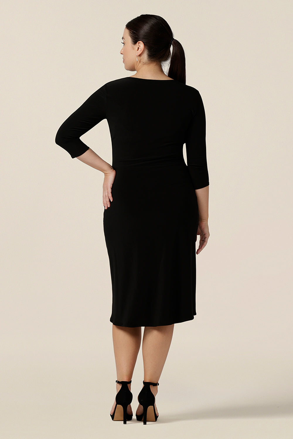 Back view of a classic black dress for evening and occasion wear, this is a fixed wrap, black jersey dress with 3/4 sleeves. Worn by a size 10 woman, shop this made-in-Australia dress is by Australian and New Zealand women's clothes label, Leina & Fleur and is available to shop in dress sizes 8 to 24.