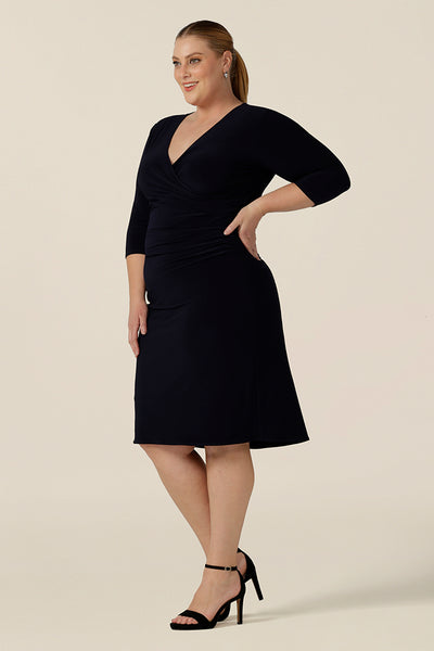 Side view of an elegant navy blue dress for evening and occasion wear, this is a fixed wrap, navy jersey dress with 3/4 sleeves. Shown for plus sizes in size 18 , this made-in-Australia dress is by Australian and New Zealand women's clothes label, Leina & Fleur and is available to shop in dress sizes 8 to 24.
