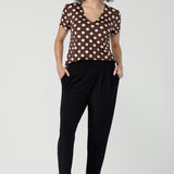 Size 10 woman wearing a brown polka dot top and black work pants with brown spotty heels.