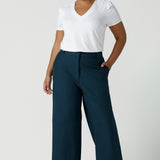 Size 16 woman wears the Yael pant in Petrol. A high waist tailored pant with tailoring elements like side pockets, zip front and belt loops. Full length wide leg pant suitable for comfortable workwear with a statement Petrol colour. Styled back with white Evan top in white bamboo. Made in Australia for women size 8 - 24.