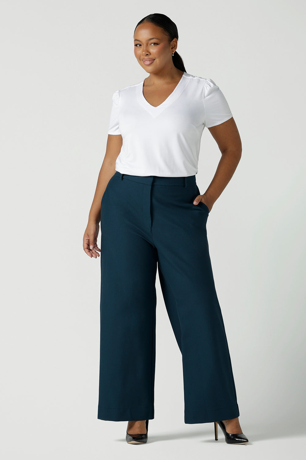 Size 16 woman wears the Yael pant in Petrol. A high waist tailored pant with tailoring elements like side pockets, zip front and belt loops. Full length wide leg pant suitable for comfortable workwear with a statement Petrol colour. Styled back with white Evan top in white bamboo. Made in Australia for women size 8 - 24.