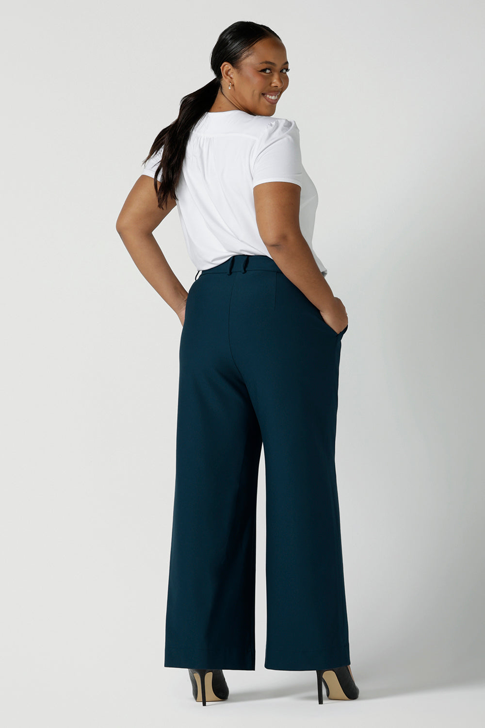 Back view of a size 16 woman wears the Yael pant in Petrol. A high waist tailored pant with tailoring elements like side pockets, zip front and belt loops. Full length wide leg pant suitable for comfortable workwear with a statement Petrol colour. Styled back with white Evan top in white bamboo. Made in Australia for women size 8 - 24.