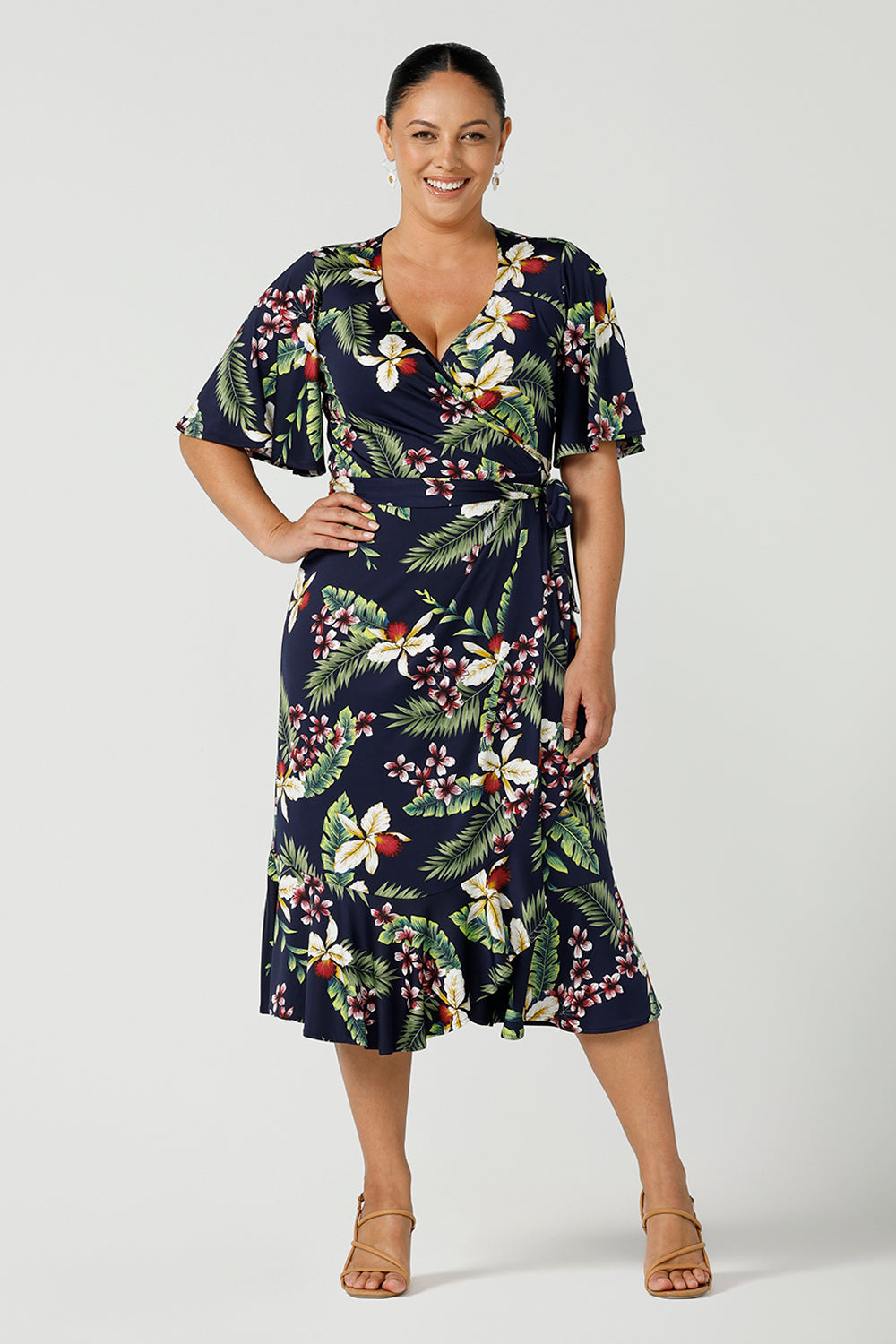 A curvy woman in a size 12 wears wrap dress for curvy women in festive Merriment Christmas tropical print. Jersey wrap dress in soft jersey fabric with frilly hem and sleeves. Made in Australia for sizes 8 - 24.