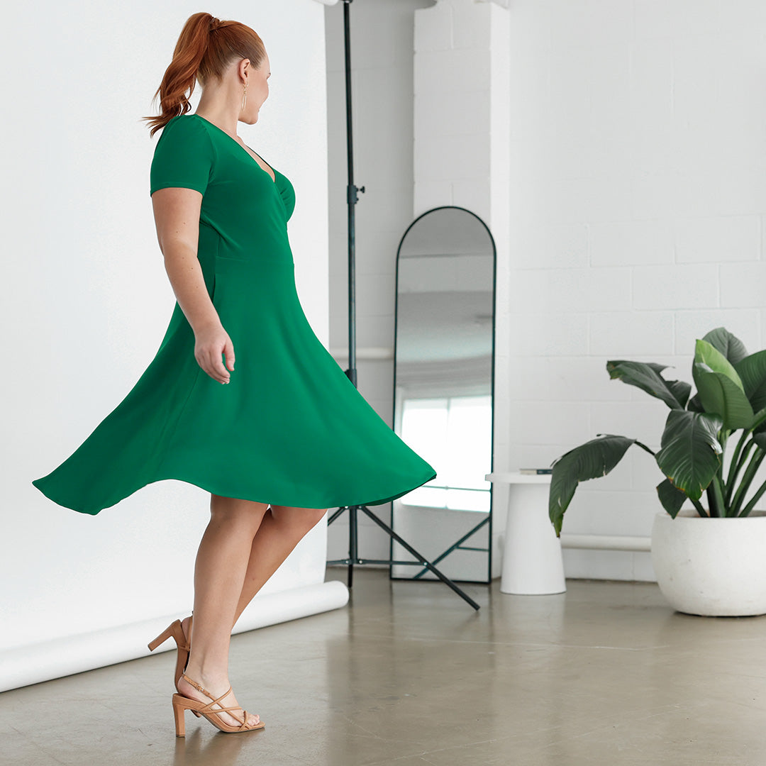 A size 12, curvy woman twirls in a short sleeve, emerald green fixed wrap dress by quality, Australian-made clothing brand, Leina & Fleur.