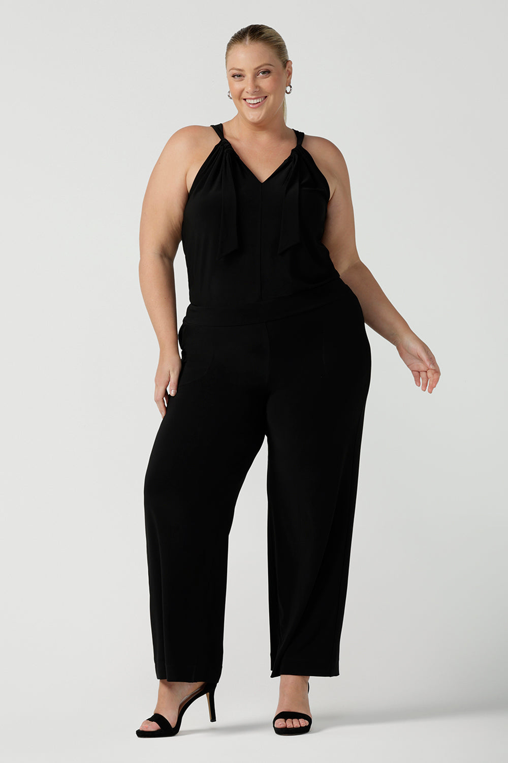 Plus size 18 women wears jumpsuit for curvy women. This black jumpsuit features a halter neck with side pockets and straight legs. Made in Australia in navy stretch jersey this jumpsuit is comfortable for work or weekend wear.  