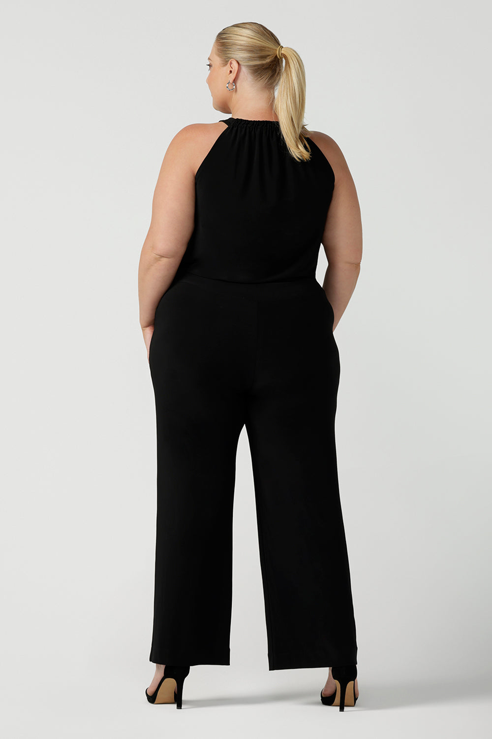 Back view of womens plus size 18 women wears jumpsuit for curvy women. This black jumpsuit features a halter neck with side pockets and straight legs. Made in Australia in navy stretch jersey this jumpsuit is comfortable for work or weekend wear.  