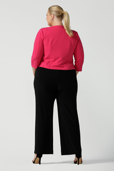 Plus size 18 women wears jumpsuit for curvy women. This black jumpsuit features a halter neck with side pockets and straight legs. Made in Australia in navy stretch jersey this jumpsuit is comfortable for work or weekend wear.  Styled with a pink workwear jacket. 