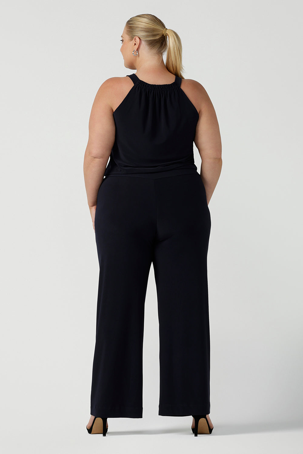 Curvy woman wears jumpsuit in size 18. This navy jumpsuit features a halter neck with side pockets and straight legs. Made in Australia in navy stretch jersey this jumpsuit is comfortable for work or weekend wear.