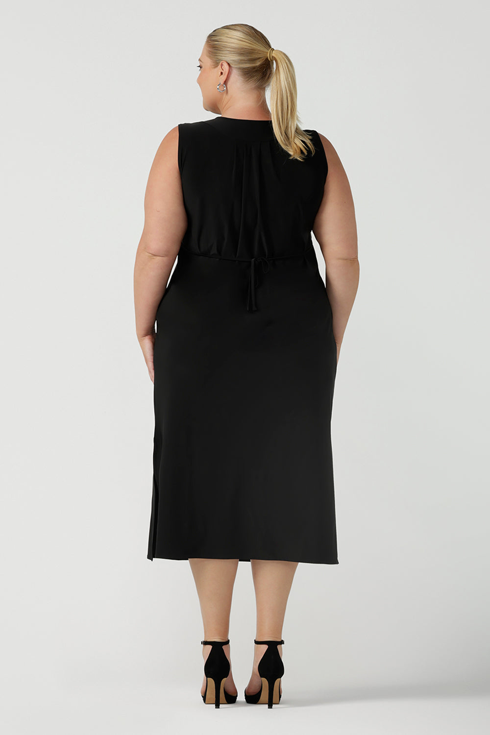 Back view of women's black dress in jersey for women. Pictured on a size 18 for petite to plus size women 8-24. Made in Australia in soft black jersey featuring a v-neckline and pleated front.